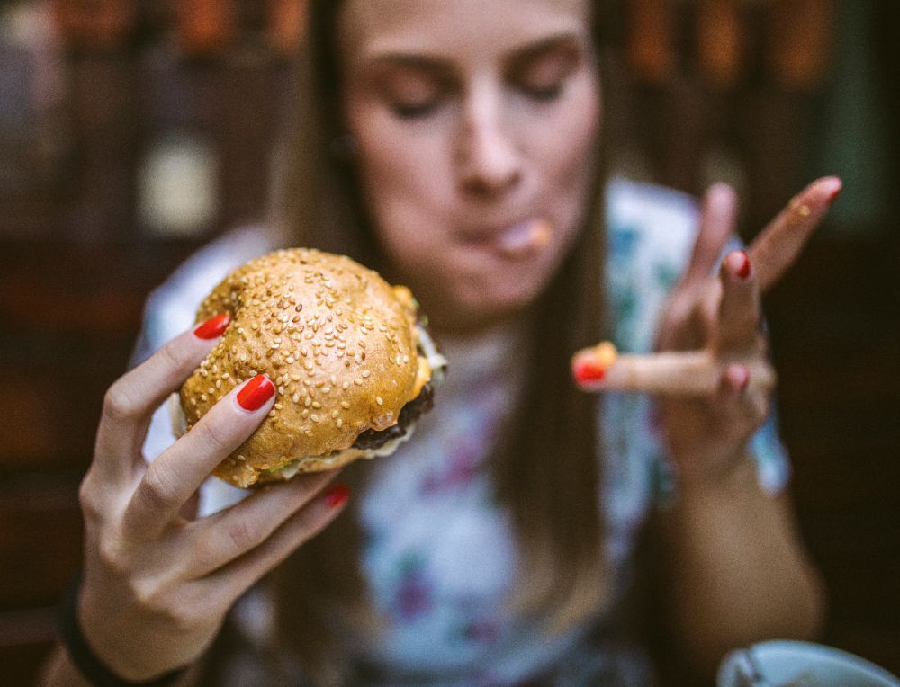 Nainen herkuttelee hampurilaisella, mikä voi aiheuttaa ärtyvän suolen oireyhtymästä kärsivälle vatsavaivoja.