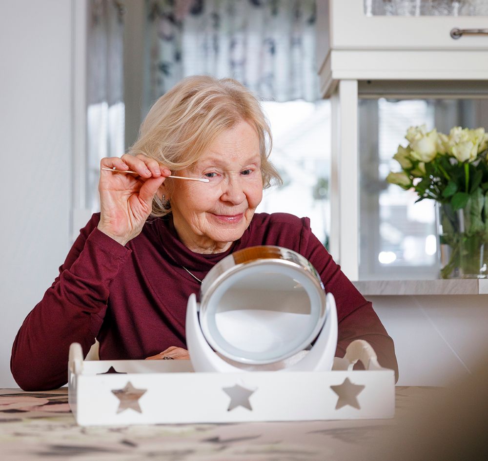 Kuvassa iäkkäämpi nainen hoitaa luomireunan tulehdusta painelemalla silmää vanupuikolla.